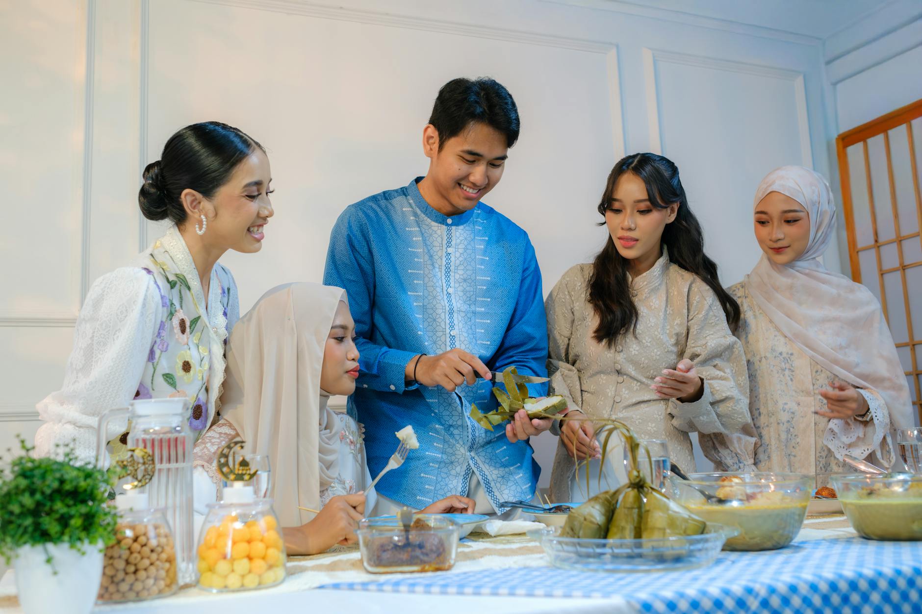 A joyful Indonesian family gathers around a table filled with festive food, celebrating Eid al-Fitr together indoors.